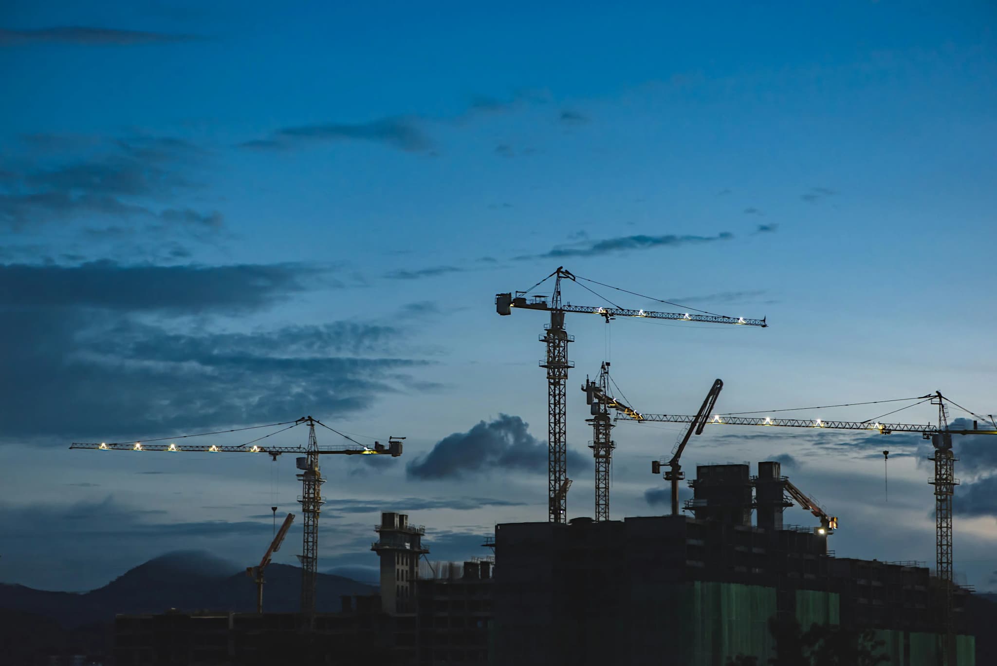 Tower cranes standing over a construction site at dusk