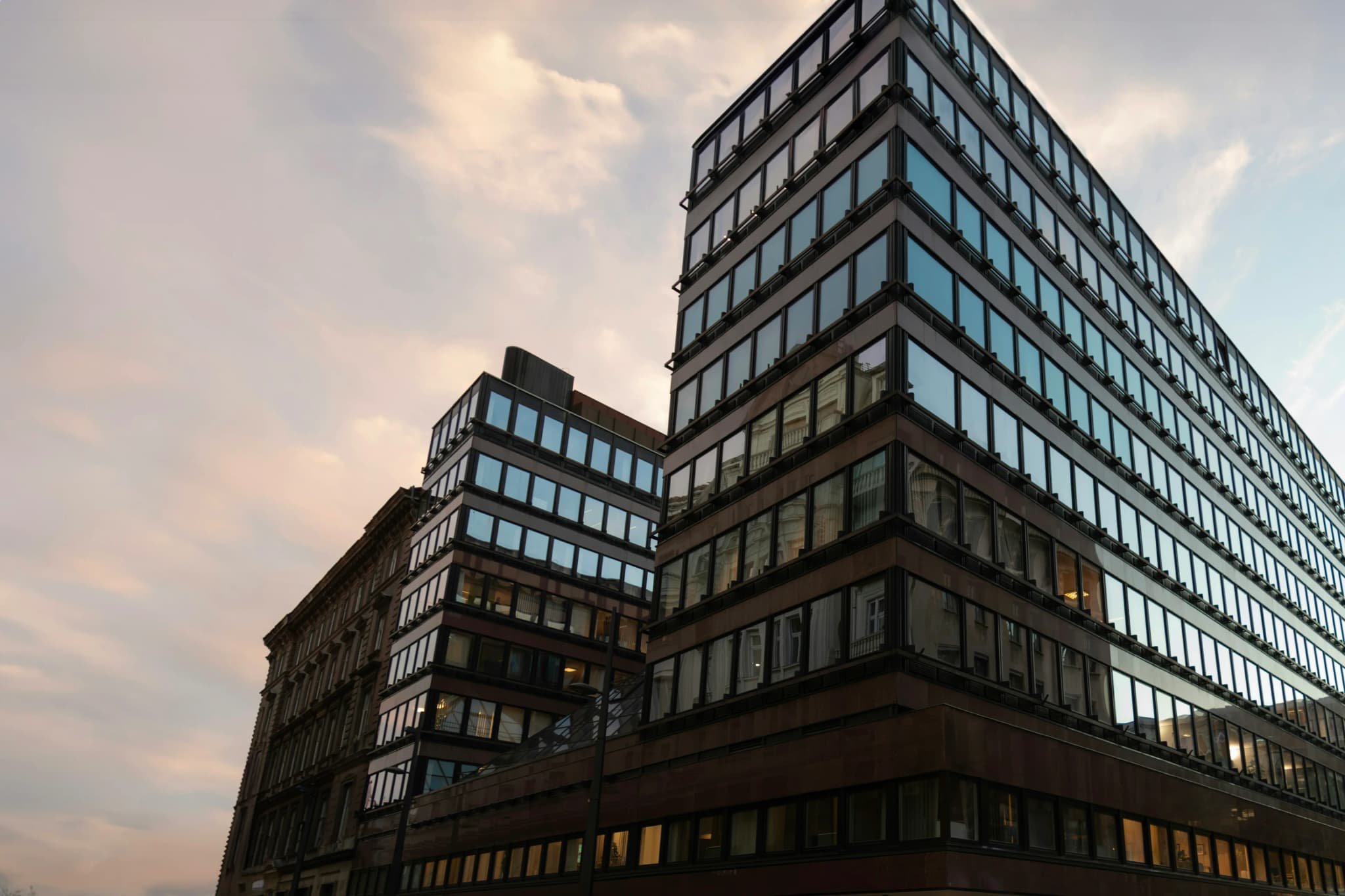 Finished office buildings at dusk, their windows lit against a clouded sky
