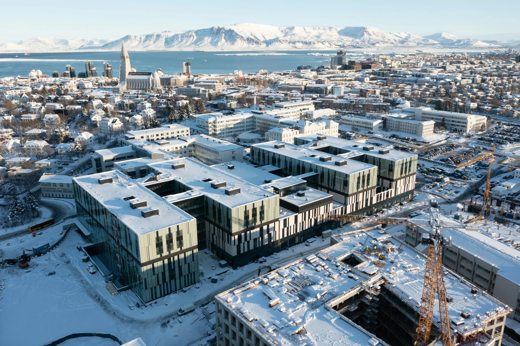 New buildings going up in a snow-covered coastal city, with the harbour and mountains behind