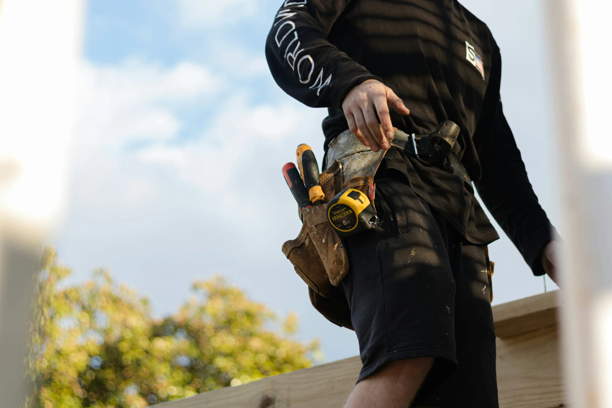 A carpenter's leather tool belt, loaded with a tape measure and hand tools